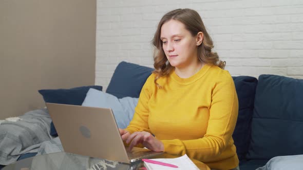 Woman in Yellow Sweater is Sitting at Desk and Working on Laptop alt