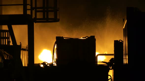 Flames Are Burning Behind the Metal Structures of an Industrial Building at Night