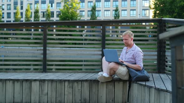 caucasian man working on a laptop near the city lake