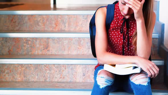 Sad schoolgirl sitting alone on staircase alt