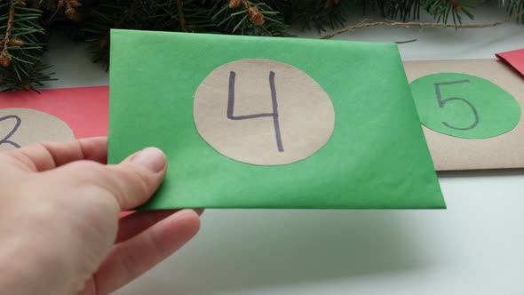 Homemade Christmas Advent Calendar Multicolored Envelopes with Numbers Lie on the Table Near Green alt