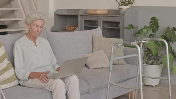 Old Lady Video Chatting on Laptop on Sofa alt