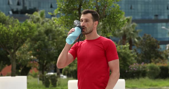Young muscular man drinking water from bottle.