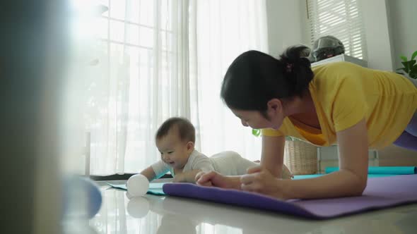 Asian Mother playing with little baby while doing yoga plank exercise