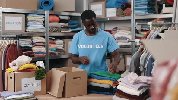 African American Volunteer Working at the Warehouse While Sorting and Iterating Clothes for alt