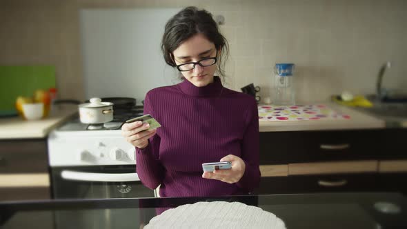 Cute Girl Sits at Home at the Table Enters the Card Number Makes an Online Purchase alt