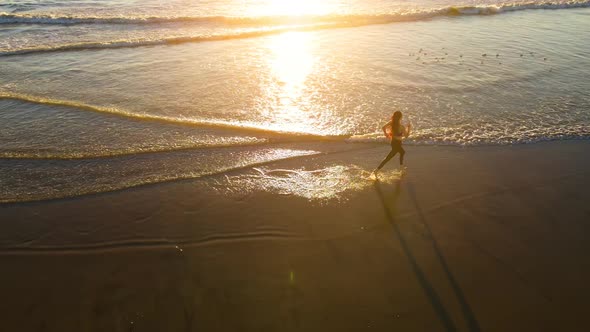 Aerial shot of fit asian woman jogging on the beach at sunset alt