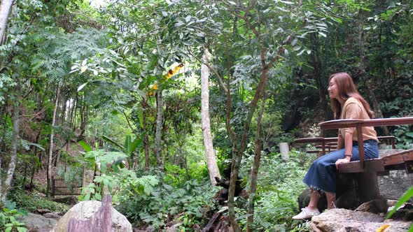 A beautiful young asian woman sitting and hanging legs in the forest