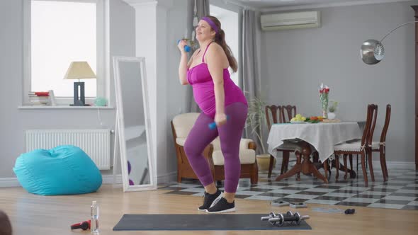Wide Shot of Cheerful Motivated Overweight Woman Having Fun Working Out with Dumbbells at Home alt