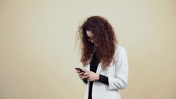 Happy Young Woman with Curly Hair Holds a Phone in Her Hand and Vb with Friends Through the Message alt