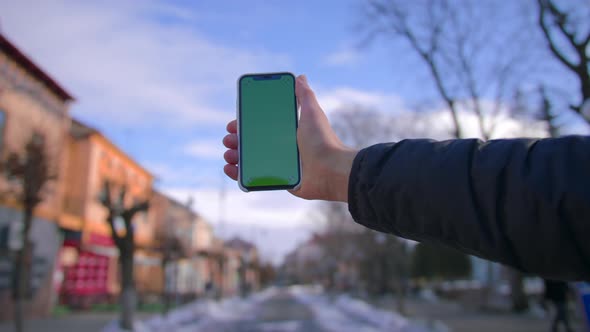 Hand Man Uses Holding a Mobile Telephone with a Vertical Green Screen Background on of Street Houses