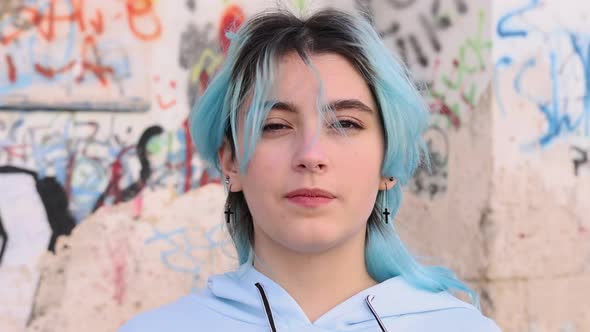 Blue haired teenage girl in light blue hoodie against graffiti wall. Head portrait alt