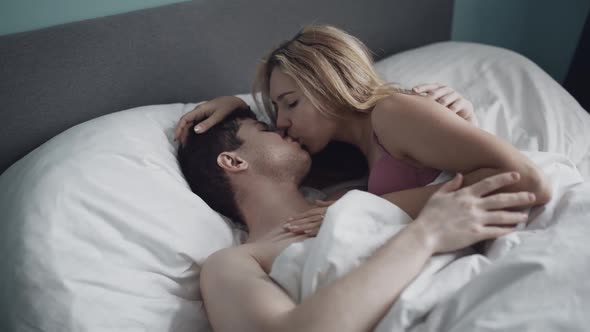 Young Woman and Man in Embrace Kissing in Bed in Bedroom alt