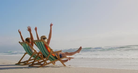 Couple with arms up relaxing on sun lounger at beach in the sunshine 4k