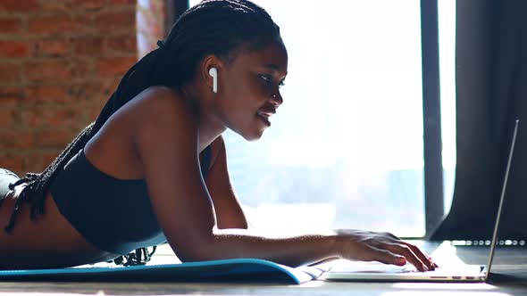 Mixed Race Nigerian Looking at Laptop Screen Making While Lying on Yoga Mat on the Floor alt