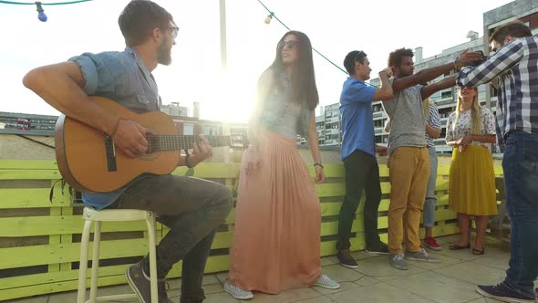 Musician playing guitar, group of people taking photos at rooftop party alt