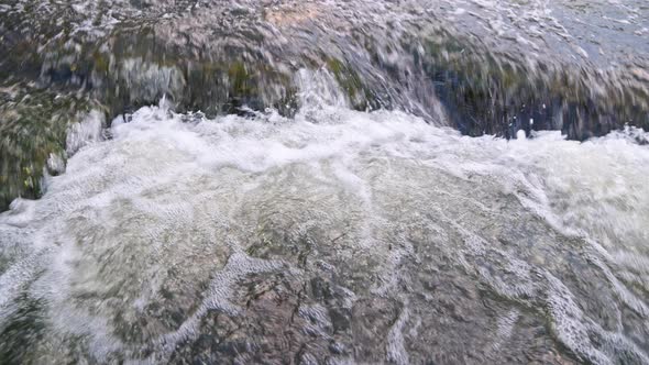 the Flowing Water of a Summer River with a Small Rapid Waterfall in Real Time at Daylight