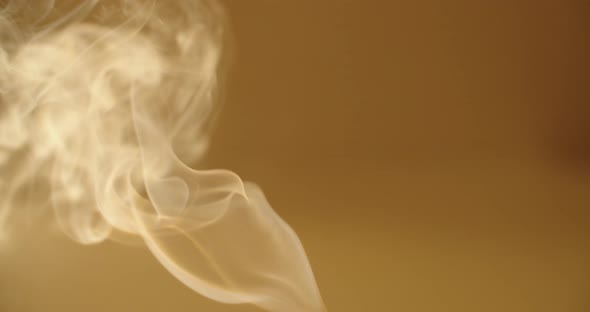 Close Up White Smoke Curling on Yellow Orange Background Slow Motion. Vapor Steaming From Incense