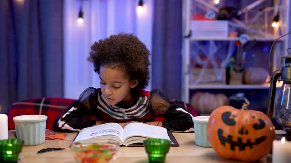 Little African American Girl in Festive Costume Reads Book with Enthusiasm alt