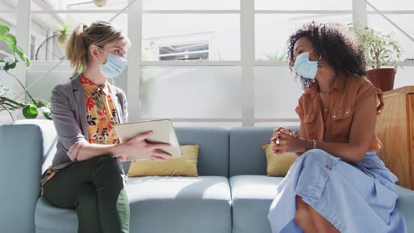 Two woman wearing face mask discussing over digital tablet at office alt
