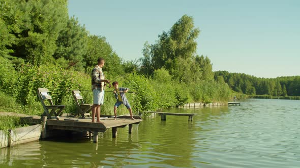 Happy Black Father and Multiethnic Boy with Spin Fishing Rods Angling From Pier alt
