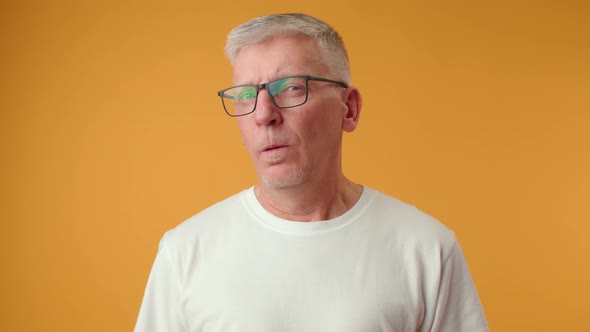 Senior Man in Glasses Have Doubts Looking Suspicious on Yellow Background
