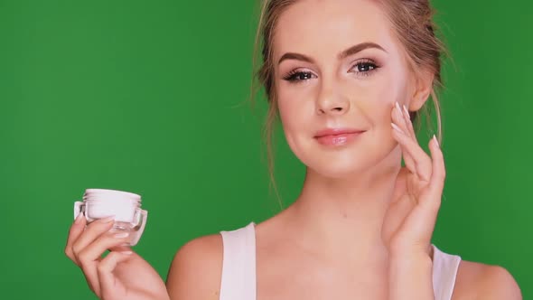 Nice Female Applying Cream on Her Cheek and Smiling in the End alt