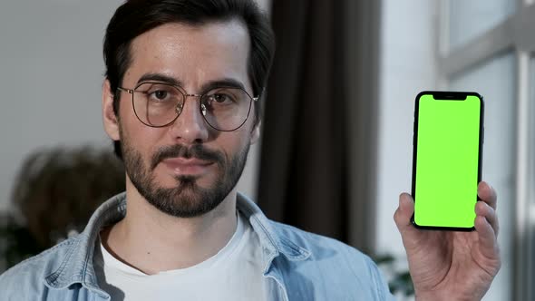 Close-Up Of a man with Glasses Using a Smartphone with a Green screen Online, Standing Near a Window alt