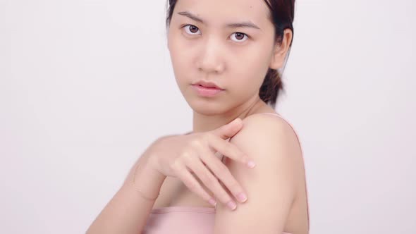 Slow motion of Asian girl with natural make up looking to camera and patting her body gently. alt