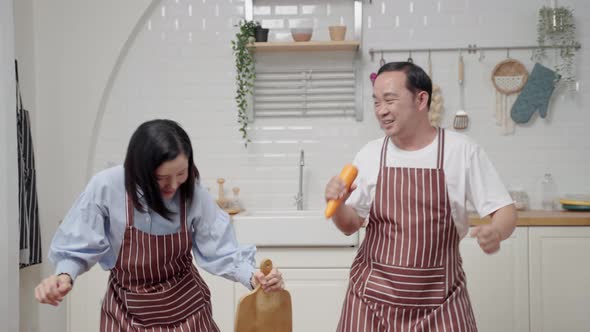 Asian husband and wife dancing while cooking in the kitchen having fun on weekends