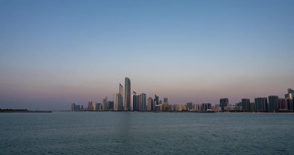 Abu Dhabi City Skyline with Skyscrapers Before Sunset with Water Reflection Day to Night Transition alt