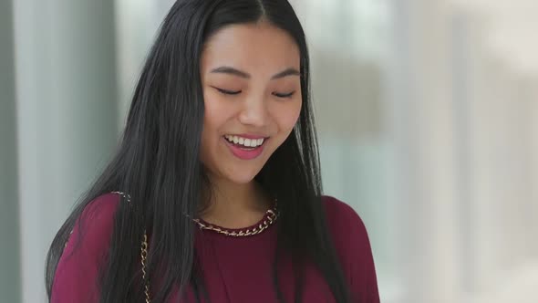 Close up of Asian woman looking at her phone and then smiling and laughing then looking back down alt