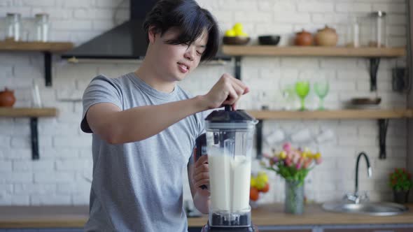 Smiling Joyful Young Man Mixing Healthful Dairy Cocktail in Blender Indoors alt