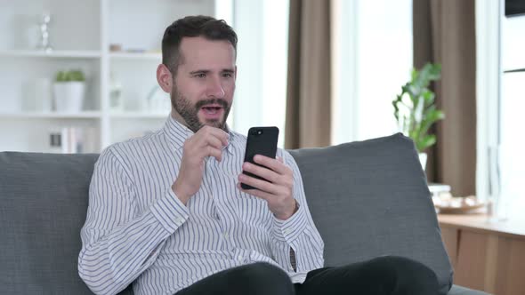 Successful Young Businessman Celebrating on Smartphone at Home  alt