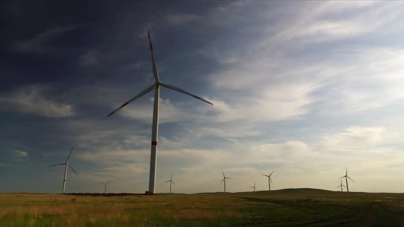 Motion the Blades of a Large Wind Turbine in a Field Against a Background of Cloudy Blue Sky with
