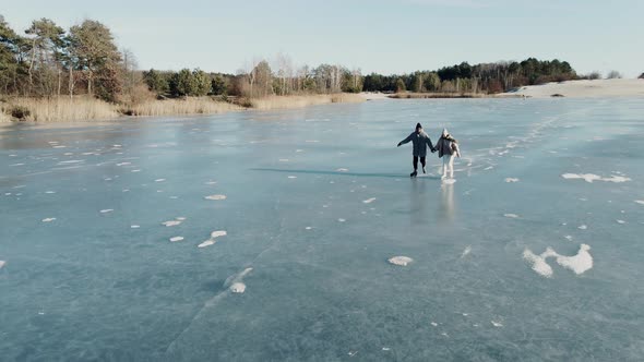 Aerial Shot of Couple Skating on a Blue Frozen Lake in Beautiful Sunny Landscape