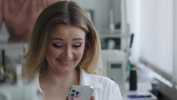 Light Hair Seamstress in the Workplace Sees Something Very Funny on Her Smartphone and and Laughs