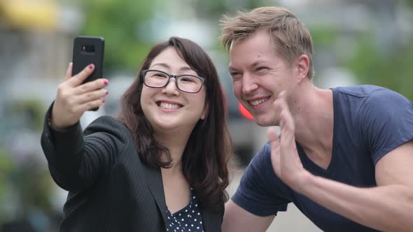 Mature Asian Businesswoman and Young Scandinavian Man Using Phone Together in the Streets Outdoors alt