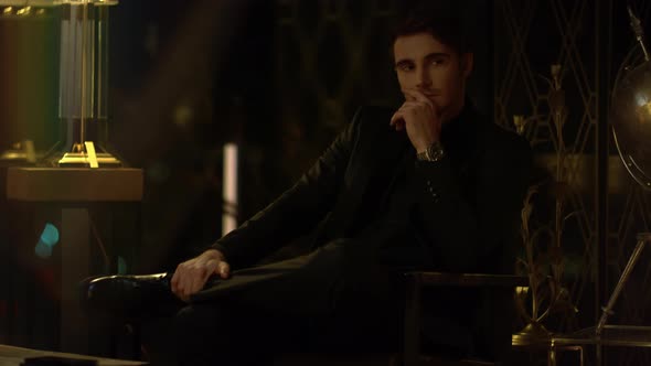 Rich Man Sitting Crossed Legs in Dark Room. Stylish Guy Contemplating Something alt