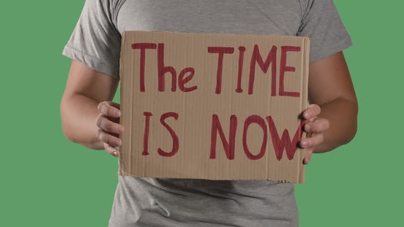 Man Holds in Front of Him a Poster From a Cardboard Box with the Words THE TIME IS NOW. Protest alt