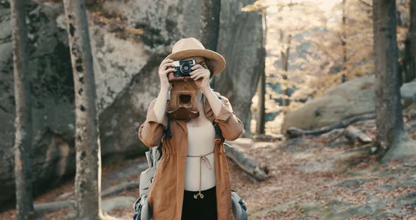 Active woman taking pictures with an vintage film camera on a forest rocks