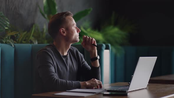 Thoughtful Serious Young Man Student Writer Sit at Home Office Desk with Laptop Thinking of alt