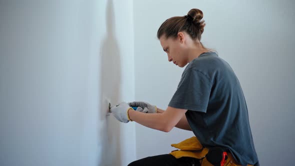 Professional Repairwoman Fixing Socket with a Screwdriver on a White Wall alt