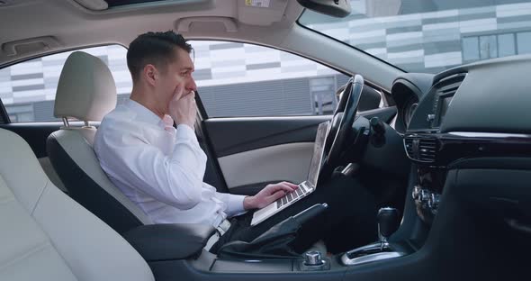Shocked Businessman Scared By Reading Bad Email on His Laptop Computer Sitting in the Driver's Seat alt