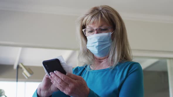 Senior woman wearing face mask wiping her smartphone with a tissue alt