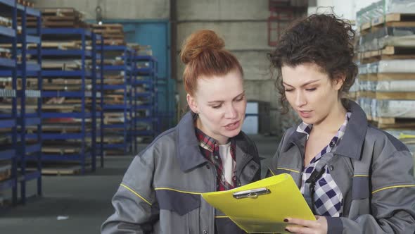 Two Female Warehouse Workers Examining Documents Together alt