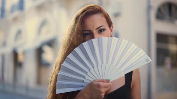 Young Elegant Redhead Woman Holding Fan in Old Town alt