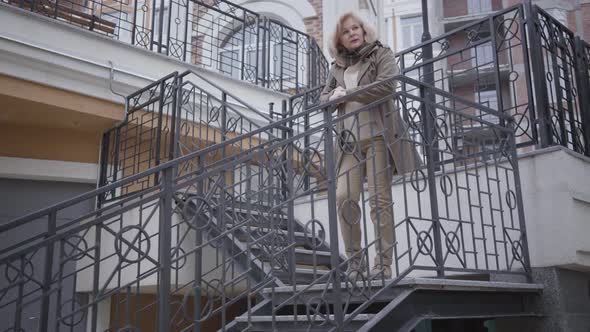 Serious Caucasian Woman Looking at Watch and Running Down the Stairs Outdoors. Confident Elegant alt