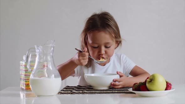 Little Cute Child Girl Eats with Pleasure Cornflakes with Milk