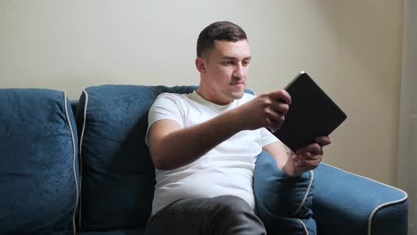 Cheerful Handsome White Man Rejoices in Victory and Laughs While Working at Tablet PC alt